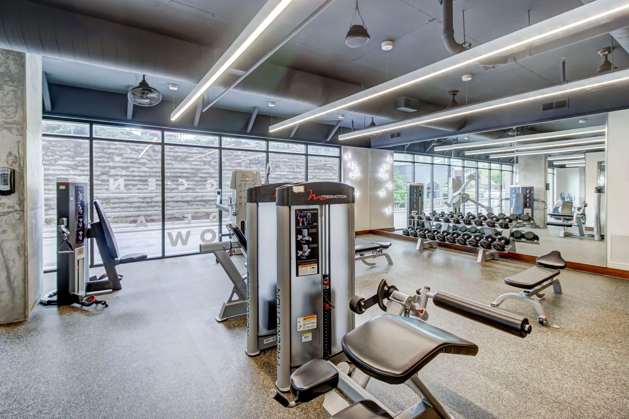 Fitness center with various weight machines, benches, free weights, large mirror wall, and floor to ceiling exterior windows